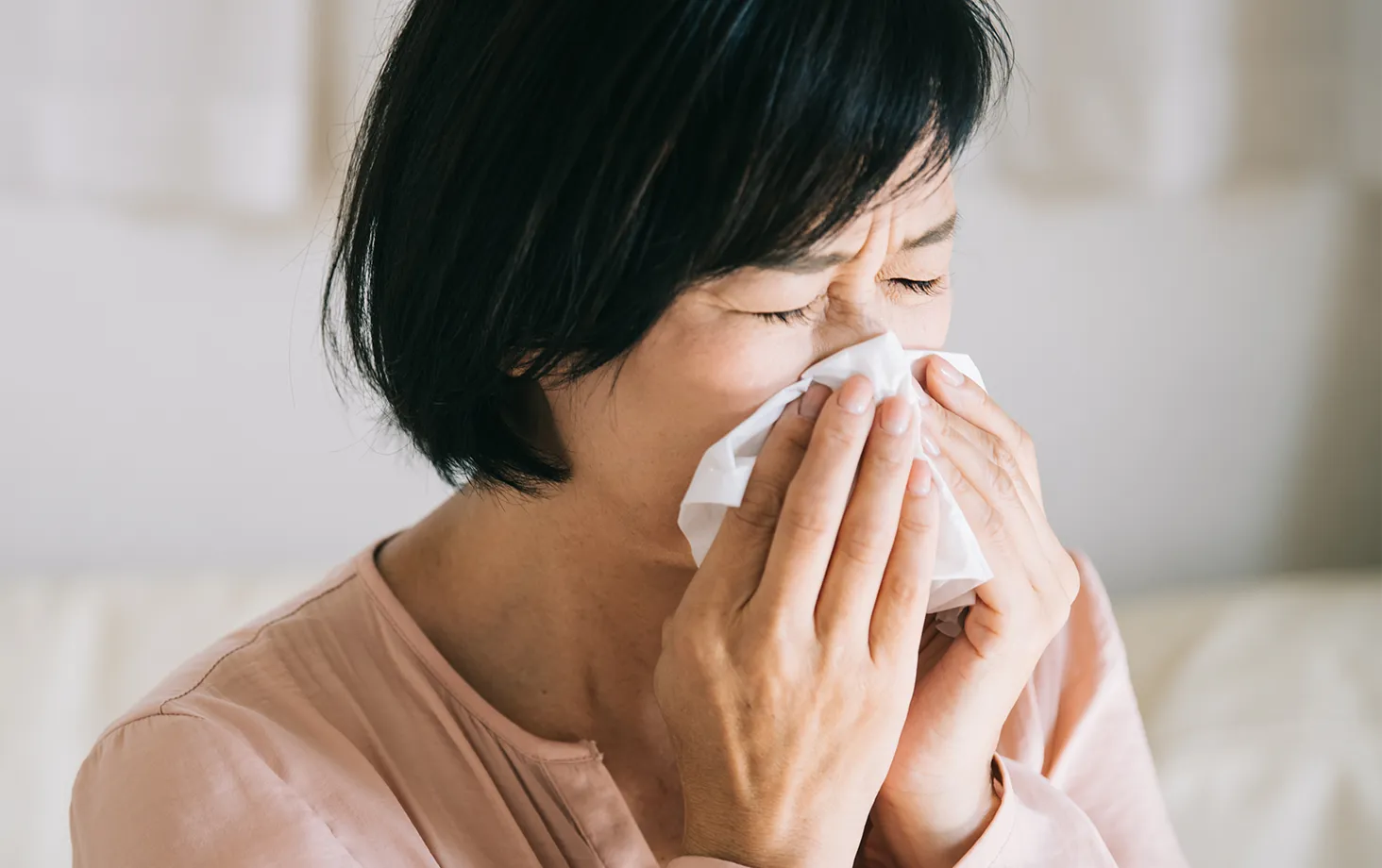 くしゃみをして鼻を押さえる女性。腹圧性尿失禁の典型的な場面