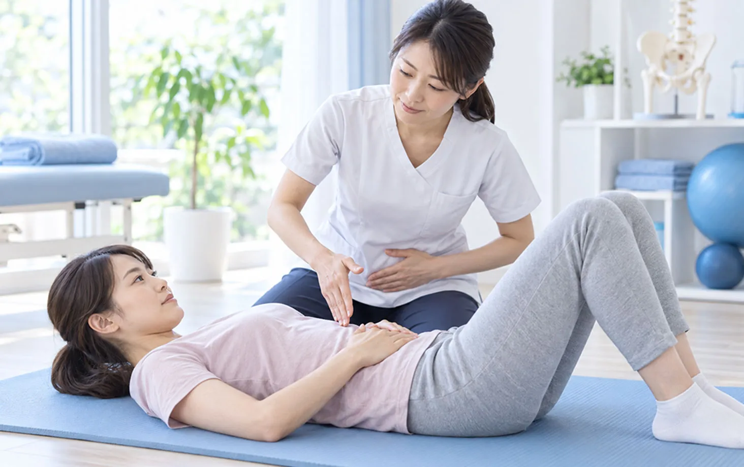 仰向けの女性に骨盤底の収縮を指導するスタッフ