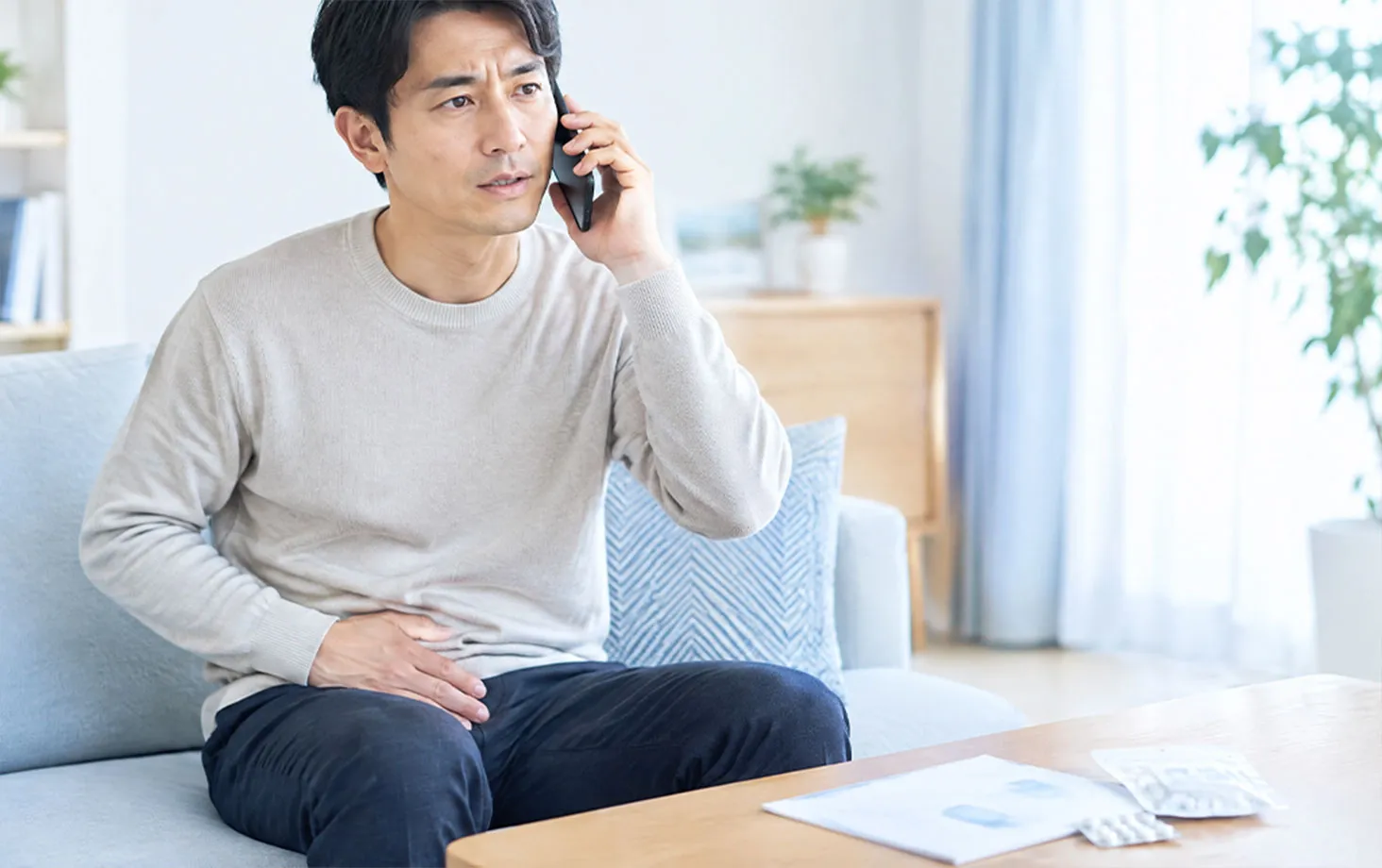 下腹部を押さえ、電話する男性